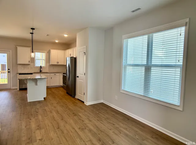 a open kitchen with stainless steel appliances granite countertop a refrigerator a sink dishwasher a stove and a large window with wooden floor