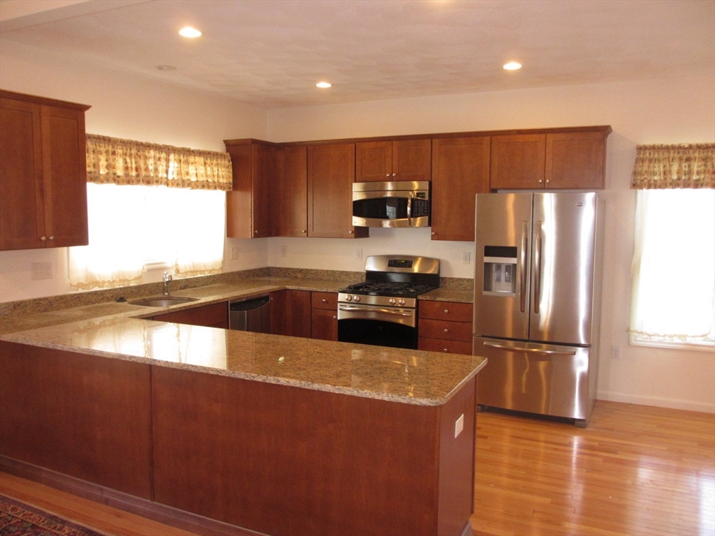 a kitchen with stainless steel appliances granite countertop a refrigerator a stove and a sink with wooden floor