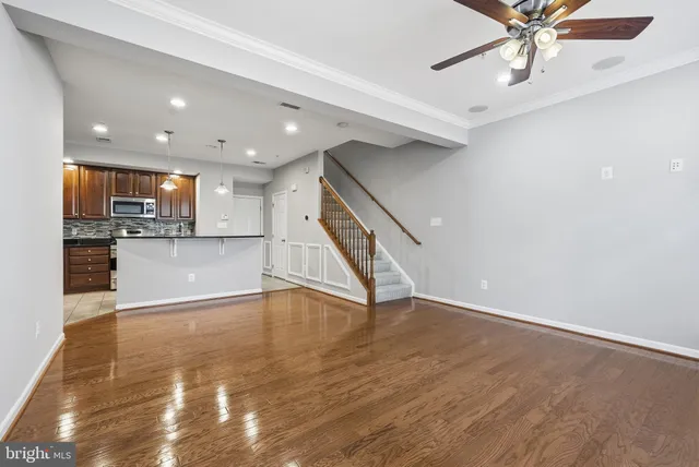 a view of an empty room with kitchen view and wooden floor