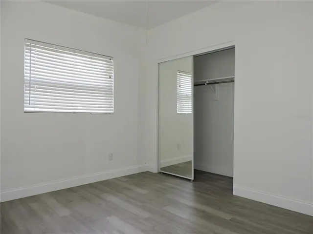 an empty room with wooden floor closet and windows