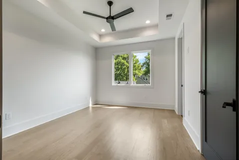 an empty room with wooden floor ceiling fan and windows