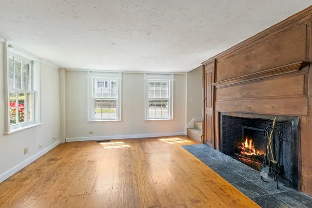 a view of an empty room with wooden floor fireplace and a window