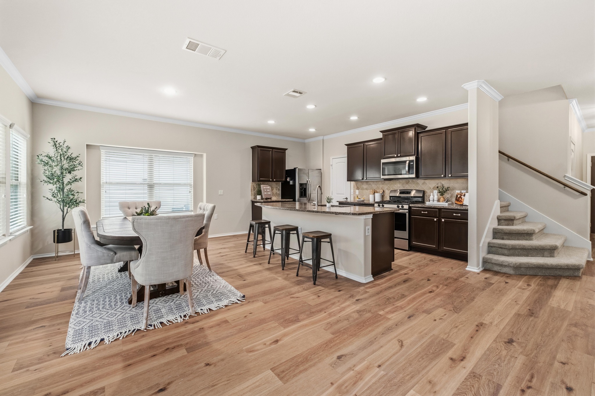 10124 Pinnacle Crest Loop Austin, TX 78747 - Photo 12 of 31 Open-concept interior featuring wood-finish flooring, a kitchen island with seating, dark wood cabinetry, stainless steel appliances, and a carpeted staircase