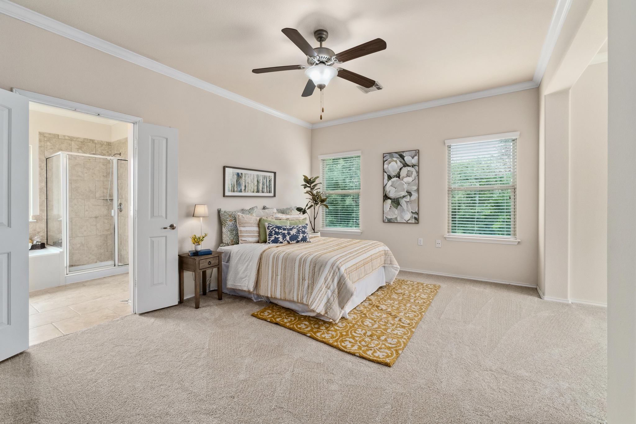10124 Pinnacle Crest Loop Austin, TX 78747 - Photo 14 of 31 Carpeted bedroom featuring a ceiling fan with integrated lighting, two windows with blinds, crown molding, and double doors opening to a full bathroom with a walk-in shower
