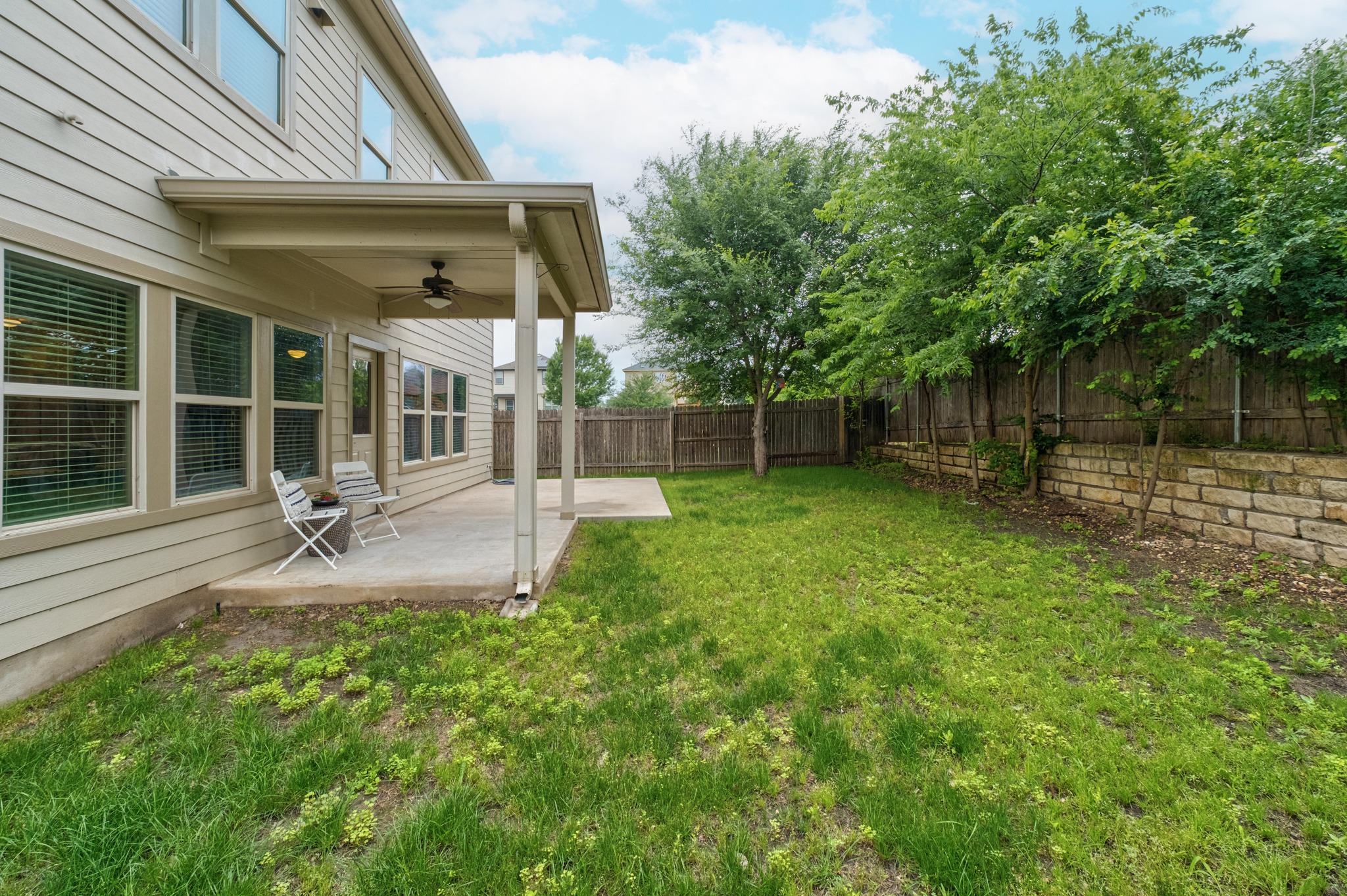 10124 Pinnacle Crest Loop Austin, TX 78747 - Photo 29 of 31 Expansive backyard featuring a covered patio with a ceiling fan, a concrete extension, a wooden privacy fence, and a stone retaining wall