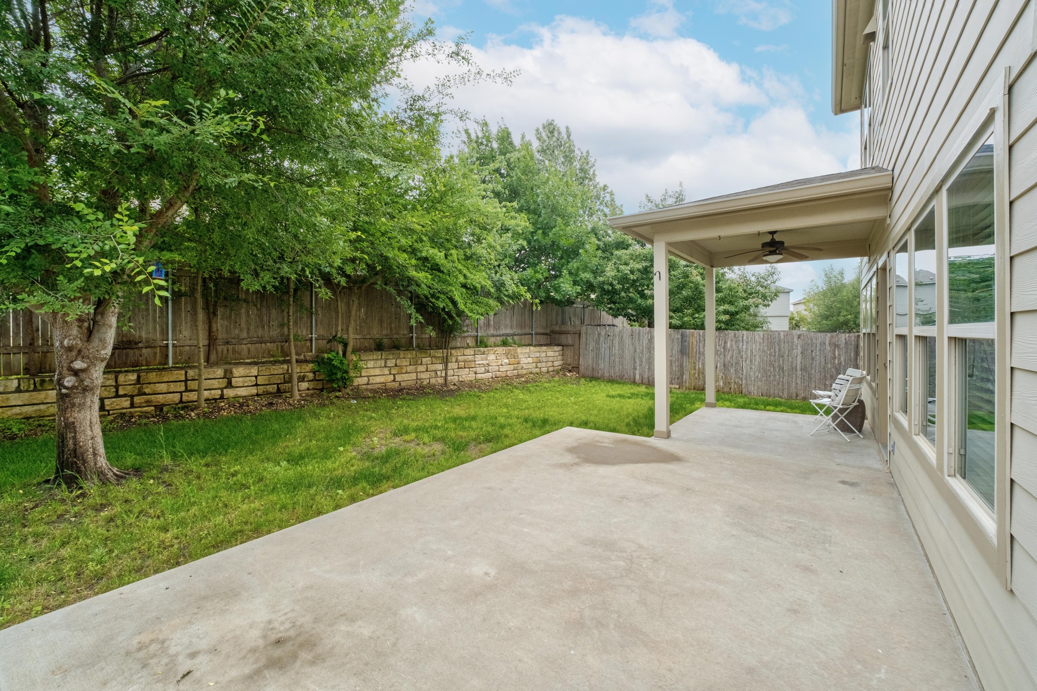 10124 Pinnacle Crest Loop Austin, TX 78747 - Photo 30 of 31 Expansive concrete patio featuring a covered portion with a ceiling fan, a lush lawn, and mature trees