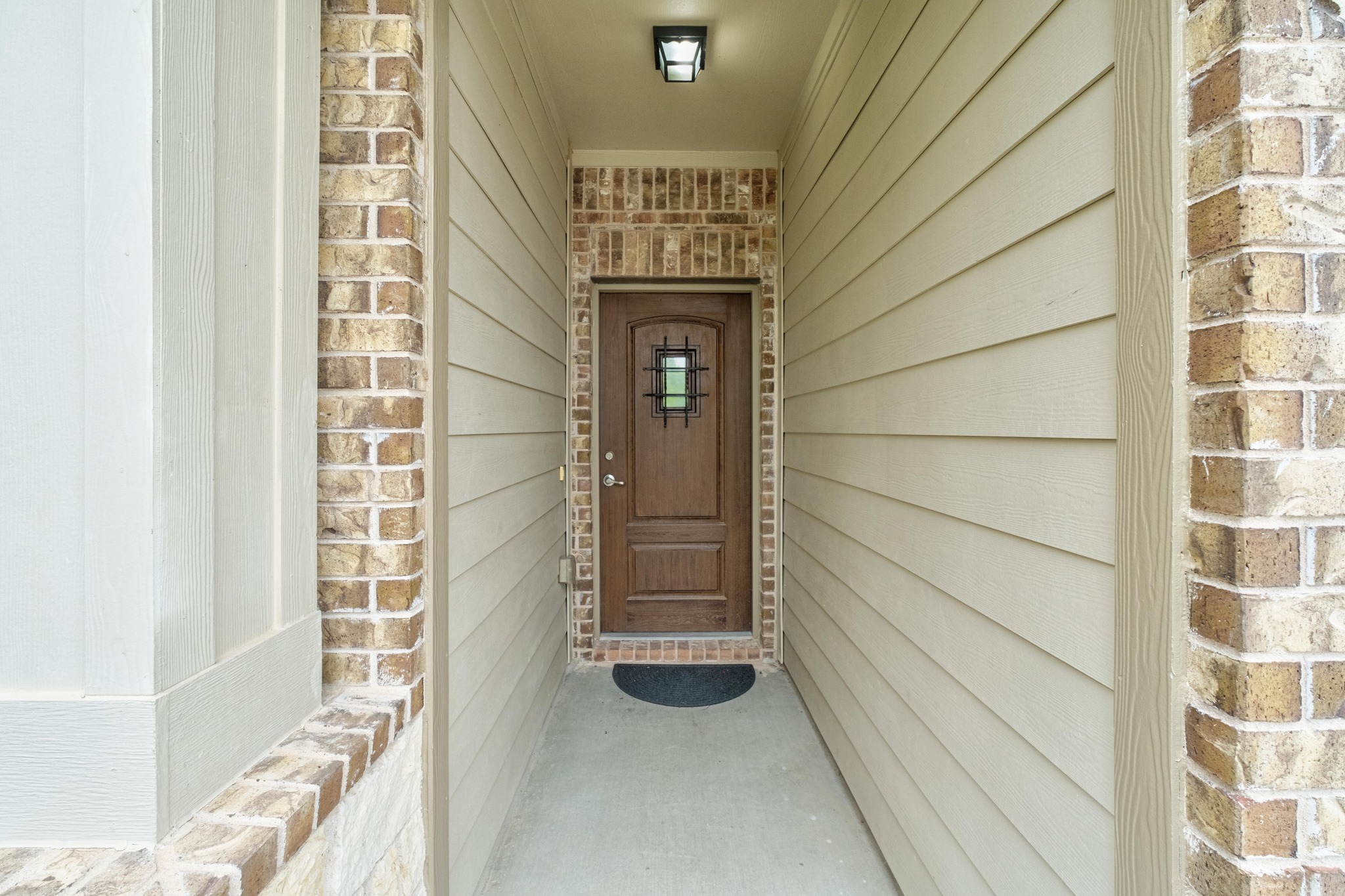 10124 Pinnacle Crest Loop Austin, TX 78747 - Photo 7 of 31 Covered entryway featuring a paneled wood-finish door with decorative ironwork, brick accents, horizontal siding, and an overhead flush-mount light fixture