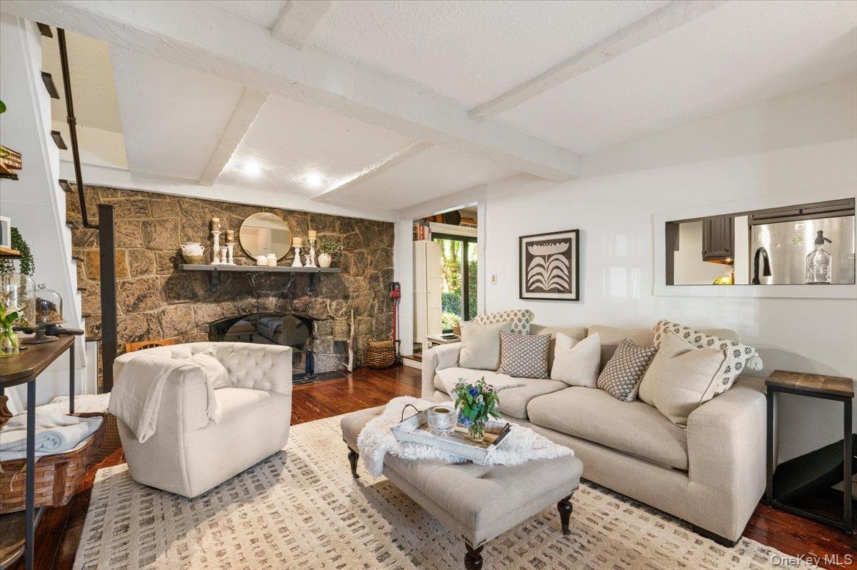 10 Rancher Place Huntington, NY 11743 - Photo 19 of 44 Spacious living area featuring a stone fireplace, wood-finish flooring, exposed ceiling beams, and a pass-through window
