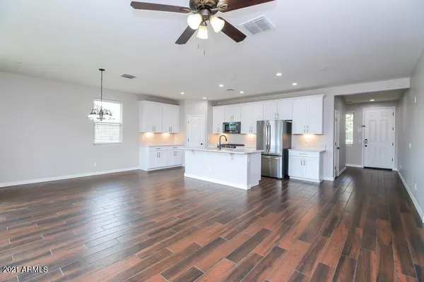 a view of an empty room and kitchen with wooden floor