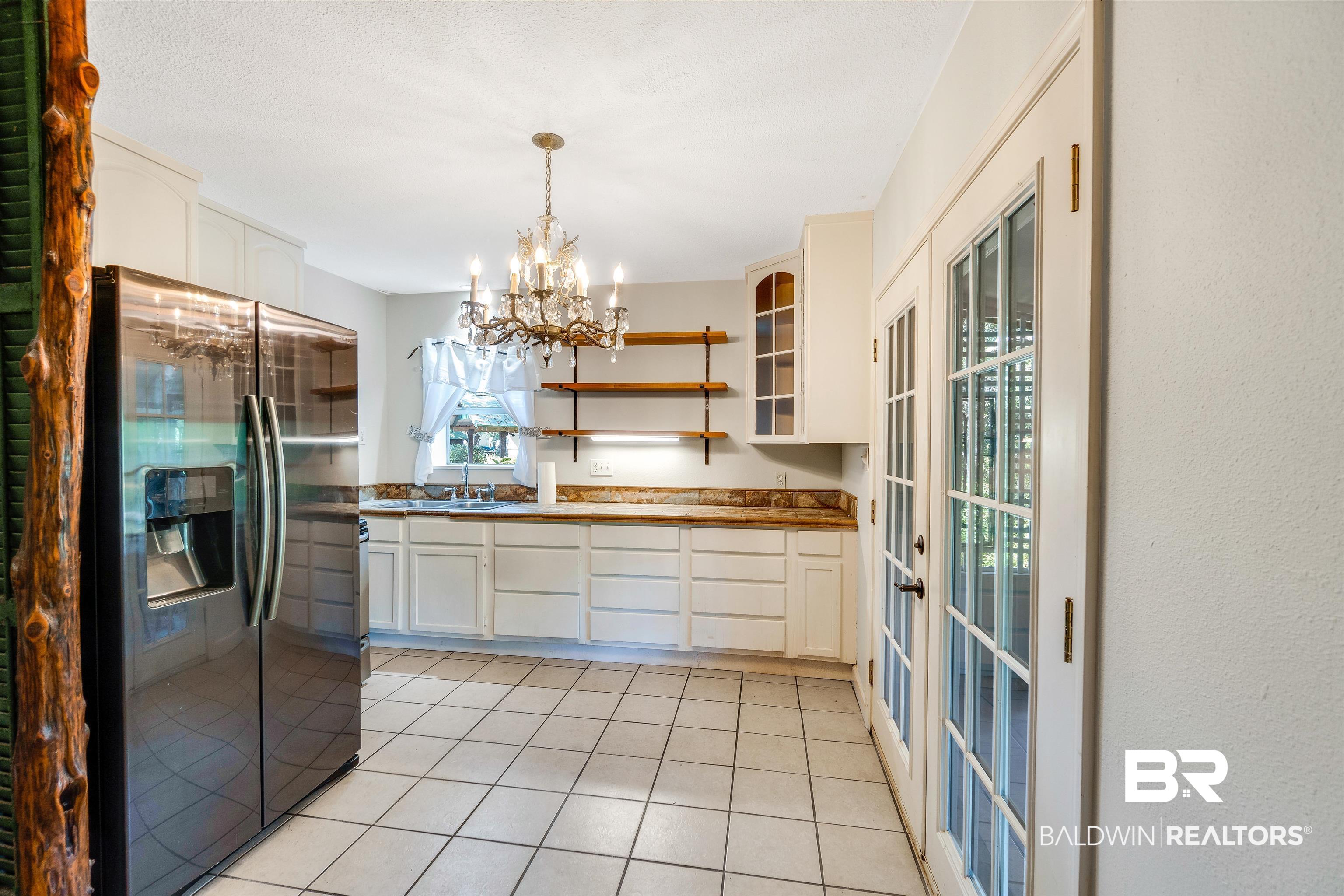 34341 Lost River Road Seminole, AL 36574 - Photo 11 of 36 Kitchen with stainless steel fridge with ice dispenser, a chandelier, light tile patterned floors, open shelves, and decorative light fixtures