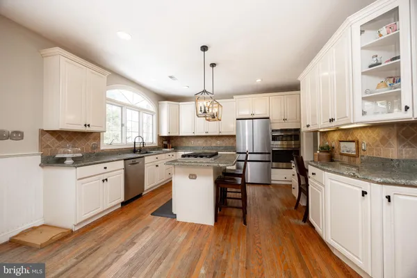 a kitchen with stainless steel appliances kitchen island granite countertop a stove top oven a sink dishwasher a dining table and chairs with wooden floor