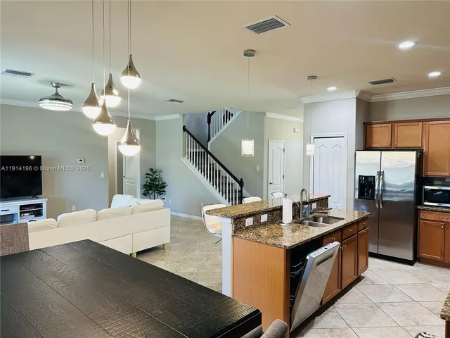 a kitchen with stainless steel appliances granite countertop a refrigerator a sink dishwasher a oven and a dining table with wooden floor