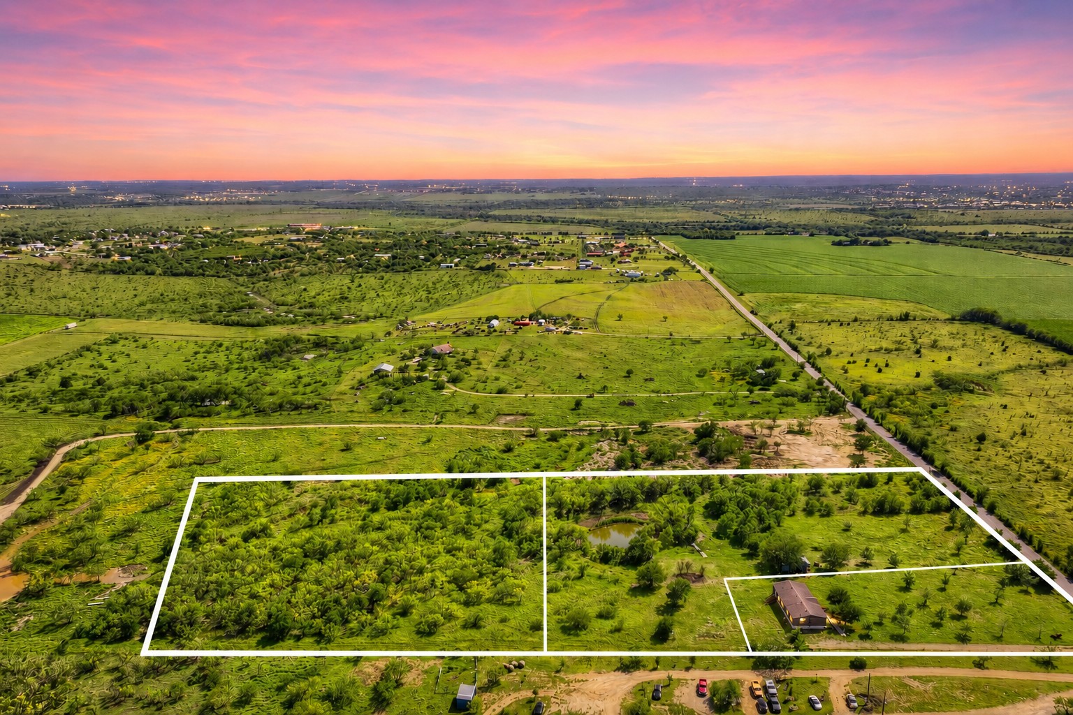 401 Graef Road Kyle, TX 78640 - Photo 1 of 30 A tranquil rural landscape unfolds with vibrant green fields and scattered residential properties, all under a dynamic sunset sky.