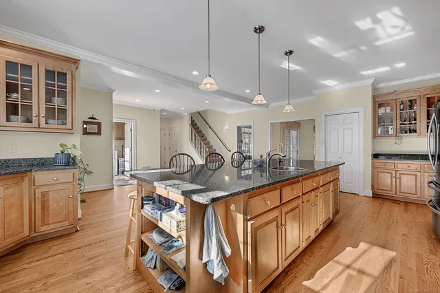 a kitchen with stainless steel appliances kitchen island granite countertop a stove a sink a refrigerator and white cabinets with wooden floor