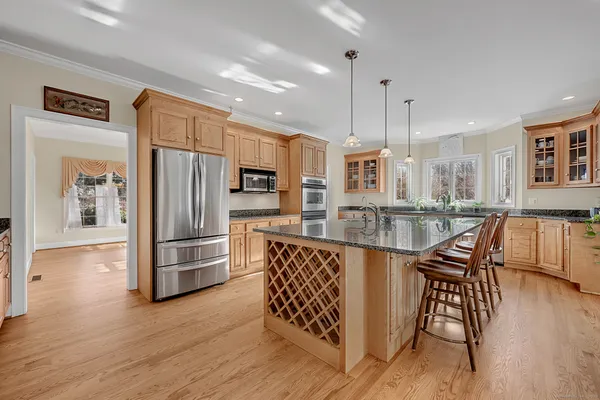 a kitchen with stainless steel appliances kitchen island granite countertop a stove a sink a refrigerator and white cabinets with wooden floor