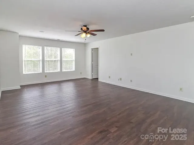 an empty room with wooden floor chandelier fan and windows