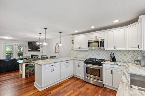 a kitchen with stainless steel appliances granite countertop a stove top oven a sink dishwasher and a microwave oven with wooden floor
