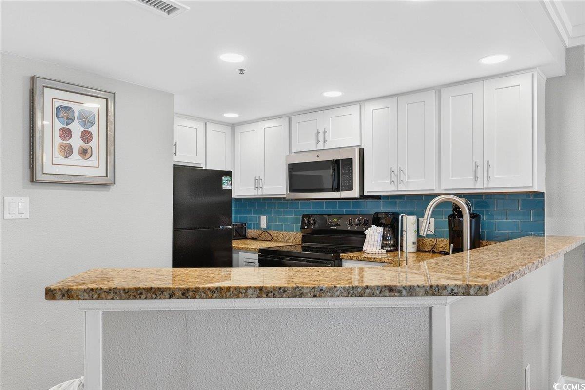 7200 North Ocean Boulevard, Unit 1155 Myrtle Beach, SC 29572 - Photo 28 of 40 Kitchen with black appliances, a peninsula, backsplash, light stone counters, and white cabinets
