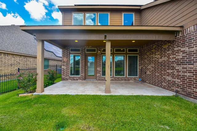 a view of a brick house with a yard plants and large tree