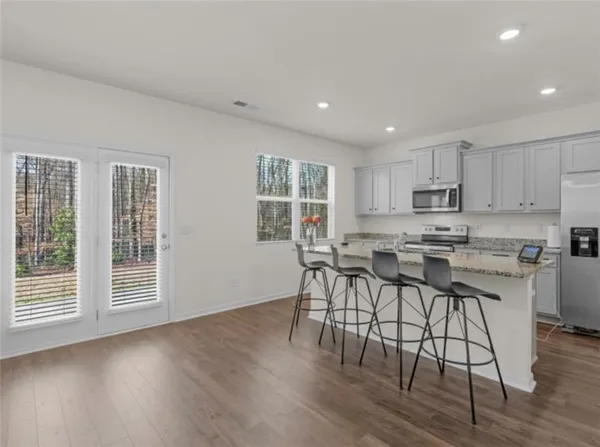a kitchen with stainless steel appliances granite countertop a stove top oven a sink a refrigerator with white cabinets and wooden floor