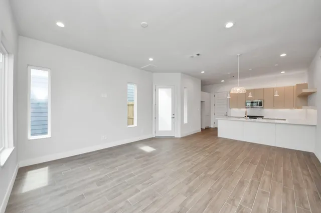 a view of an empty room and kitchen with wooden floor