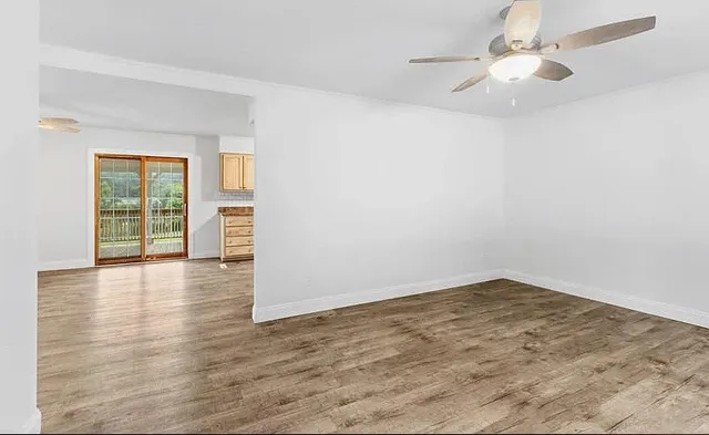 an empty room with wooden floor chandelier fan and windows