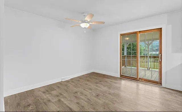 a view of a livingroom with a fan a large window with wooden floor