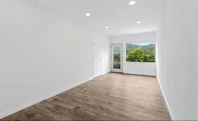 a view of an empty room with wooden floor and a window
