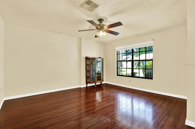an empty room with wooden floor chandelier fan and windows