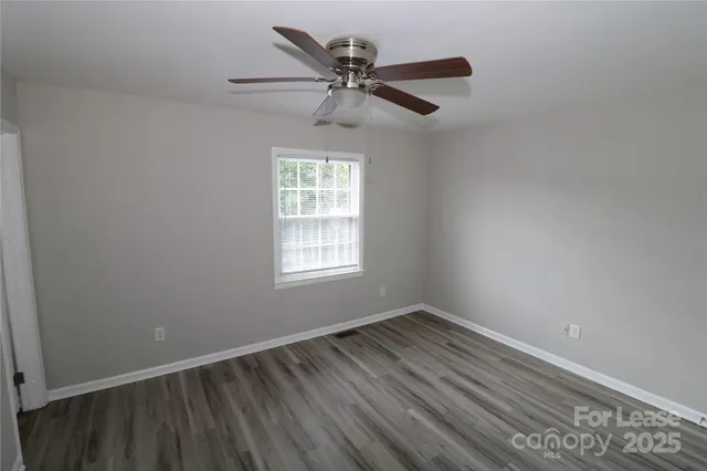 an empty room with wooden floor ceiling fan and windows