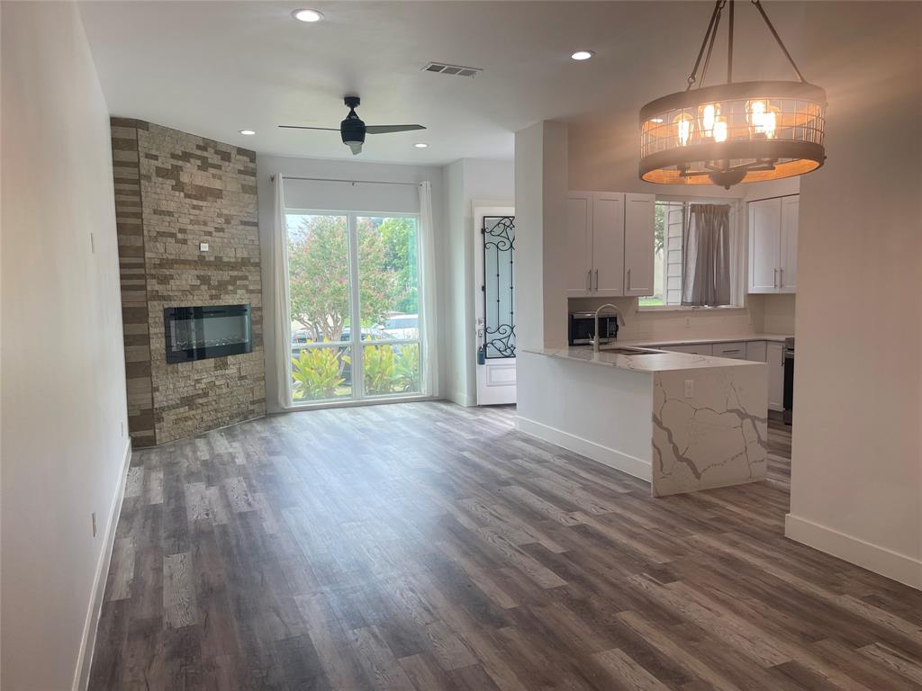 9495 Timberleaf Drive Dallas, TX 75243 - Photo 2 of 11 Kitchen featuring ceiling fan with notable chandelier, a stone fireplace, white cabinets, hardwood / wood-style floors, and decorative light fixtures
