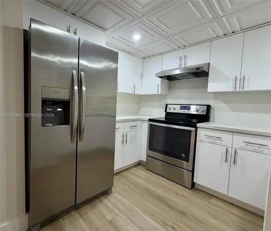 a kitchen with stainless steel appliances granite countertop a refrigerator a sink and white cabinets