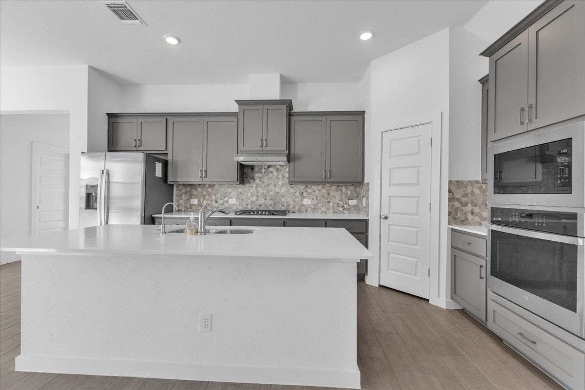 12620 Penguin Path Manor Manor, TX 78653 - Photo 9 of 37 Kitchen featuring stainless steel appliances, gray cabinetry, light wood-style flooring, tasteful backsplash, and recessed lighting