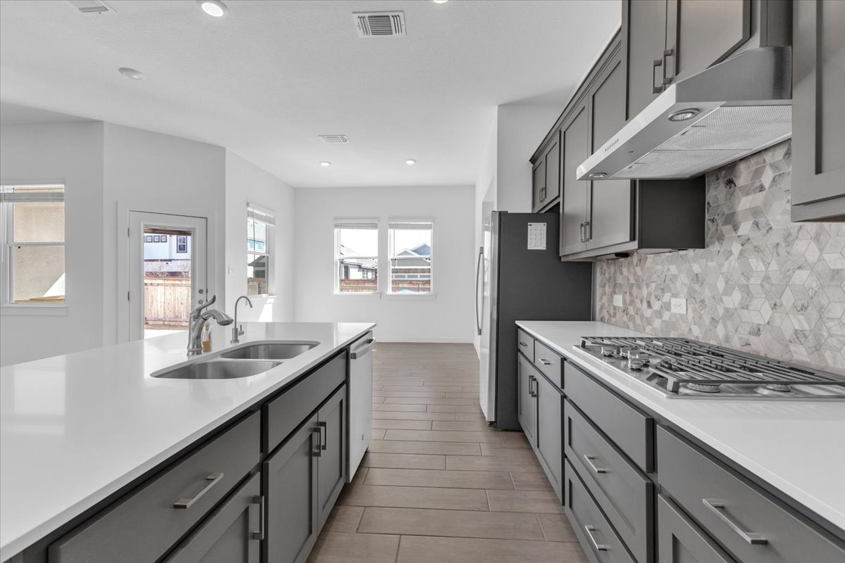 12620 Penguin Path Manor Manor, TX 78653 - Photo 11 of 37 Kitchen featuring gray cabinetry, stainless steel appliances, decorative backsplash, light stone counters, and wood finish floors