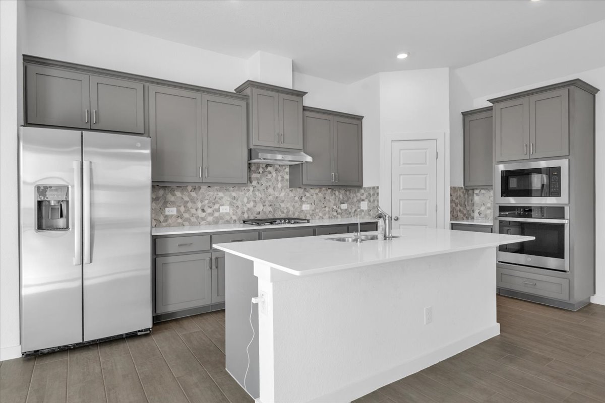 12620 Penguin Path Manor Manor, TX 78653 - Photo 13 of 37 Kitchen with stainless steel appliances, gray cabinets, a kitchen island with sink, light wood finished floors, and backsplash