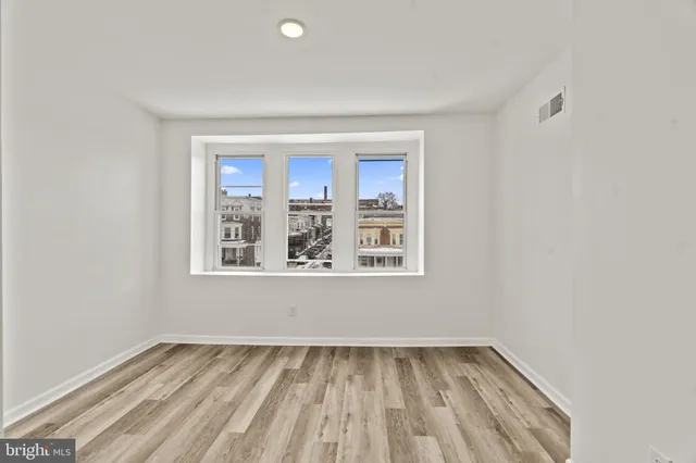 a view of an empty room with a window and wooden floor