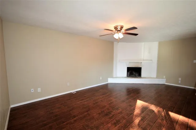 a view of a livingroom with a fireplace a ceiling fan and wooden floor