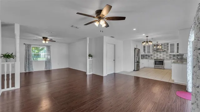 a view of an empty room with wooden floor and a kitchen