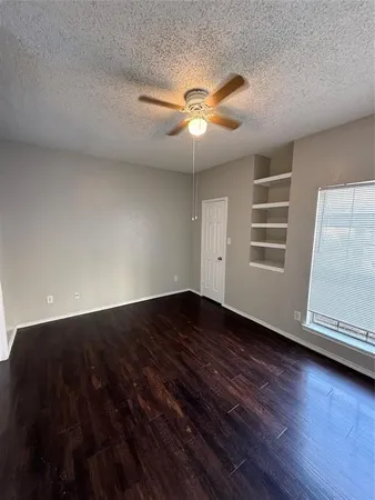 a view of an empty room with wooden floor and a ceiling fan
