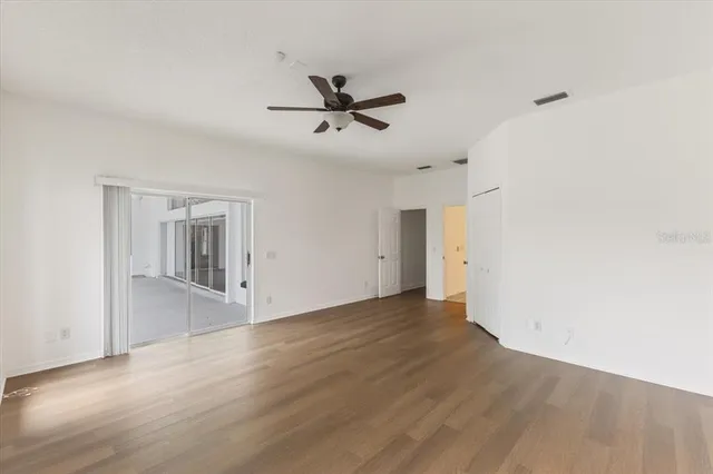 an empty room with wooden floor a ceiling fan and windows