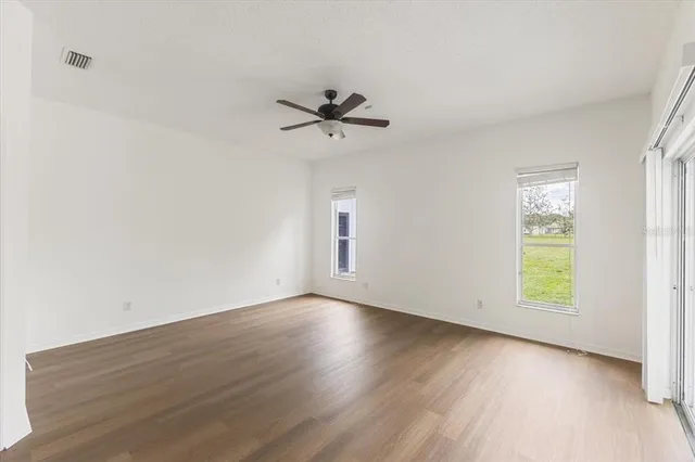 an empty room with wooden floor ceiling fan and windows