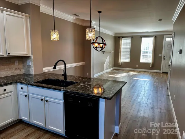 a kitchen with granite countertop a stove a sink and white cabinets with wooden floor