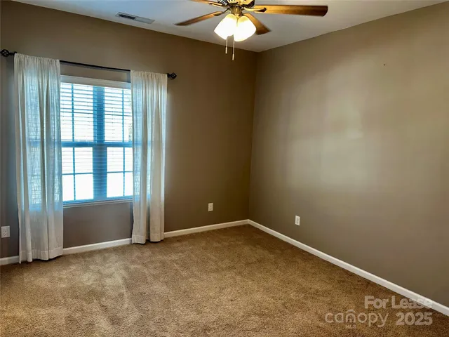 an empty room with a chandelier fan and windows