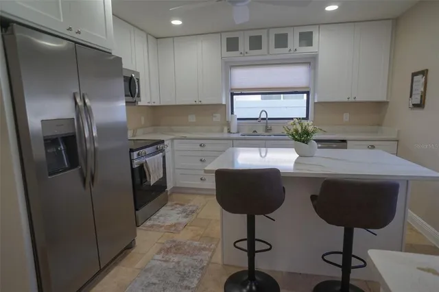 a kitchen with stainless steel appliances a stove a sink a microwave a refrigerator white cabinets and wooden floor