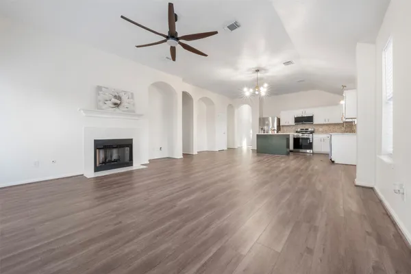 an empty room with wooden floor a ceiling fan a fireplace and windows