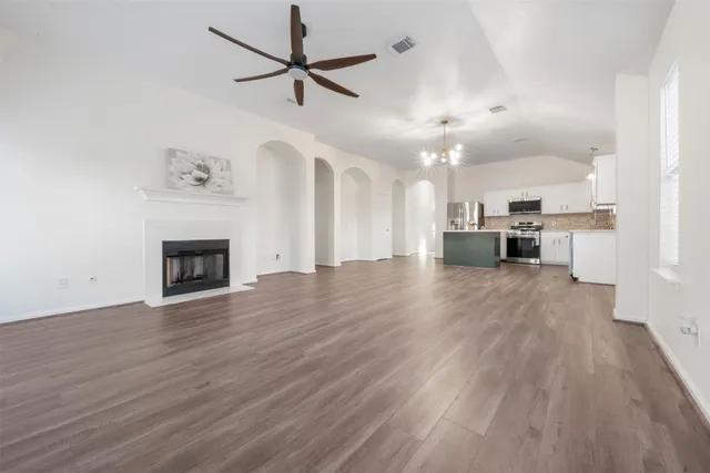 an empty room with wooden floor a ceiling fan a fireplace and windows