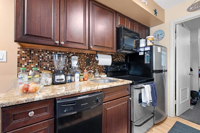 a kitchen with granite countertop stainless steel appliances a sink stove refrigerator and cabinets