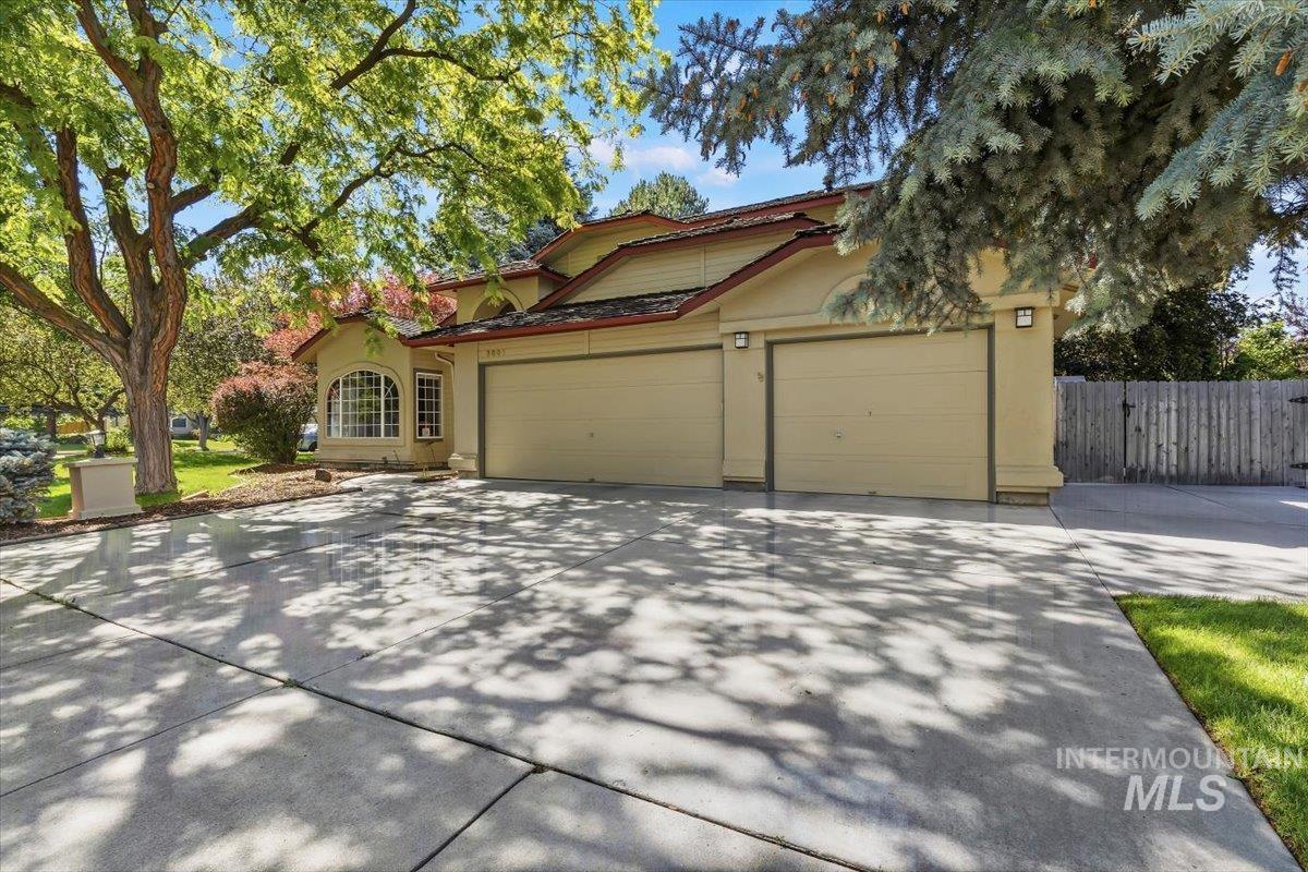 8001 West Innsbrook Court Boise, ID 83704 - Photo 4 of 39 Exterior featuring a light-colored stucco finish, multi-car garage, arched window, mature trees, and a wooden fence