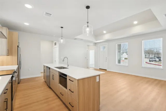 a large white kitchen with a large counter top space a sink stainless steel appliances and cabinets