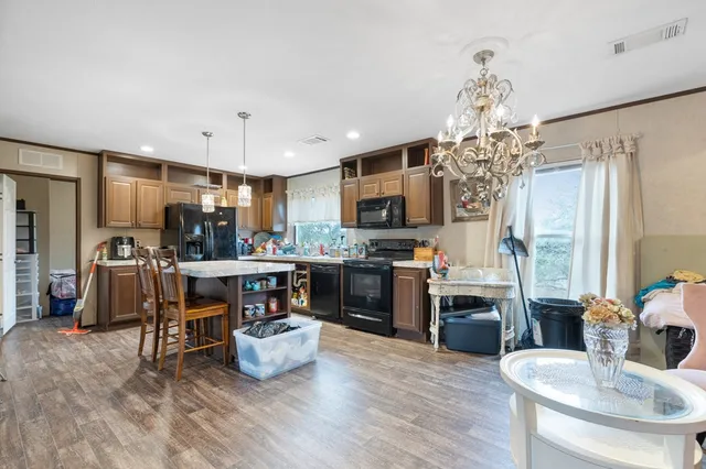 a kitchen with stainless steel appliances kitchen island granite countertop a refrigerator a stove top oven a sink dishwasher and white cabinets with wooden floor